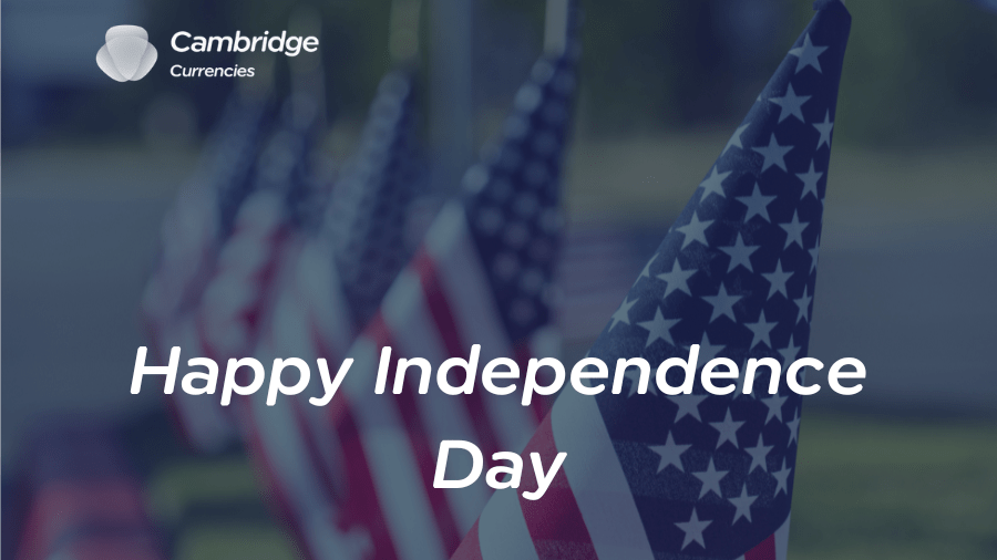 A festive image celebrating Independence Day featuring several American flags in the background, slightly blurred to create a depth effect. The foreground includes the text 'Happy Independence Day' in white letters. The Cambridge Currencies logo is positioned at the top left corner, adding a corporate touch to the holiday greeting.