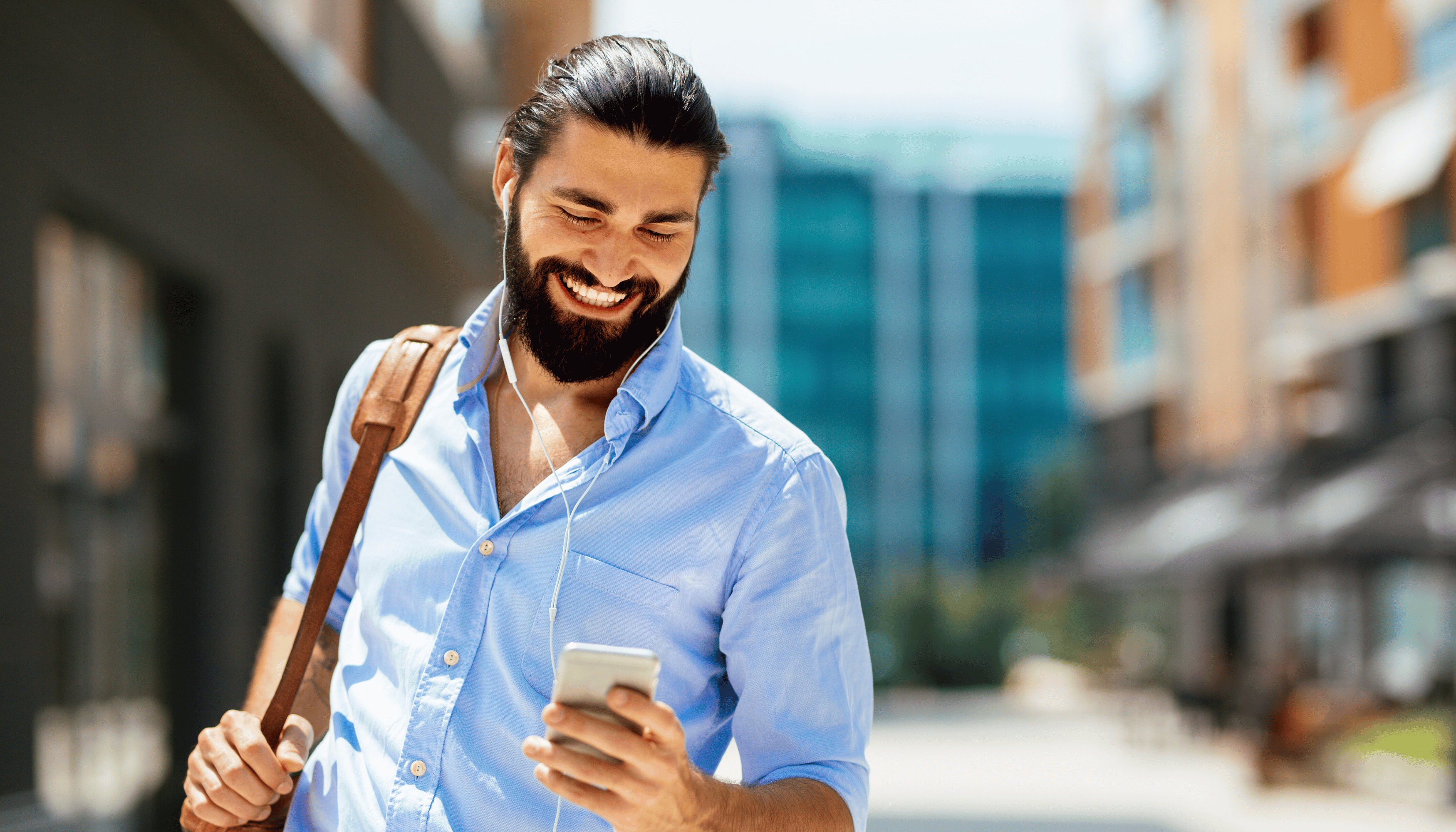 Smiling man with a beard using his smartphone while walking in an urban setting, suggesting getting the best uk pound to Indian rupee Exchnage rate.