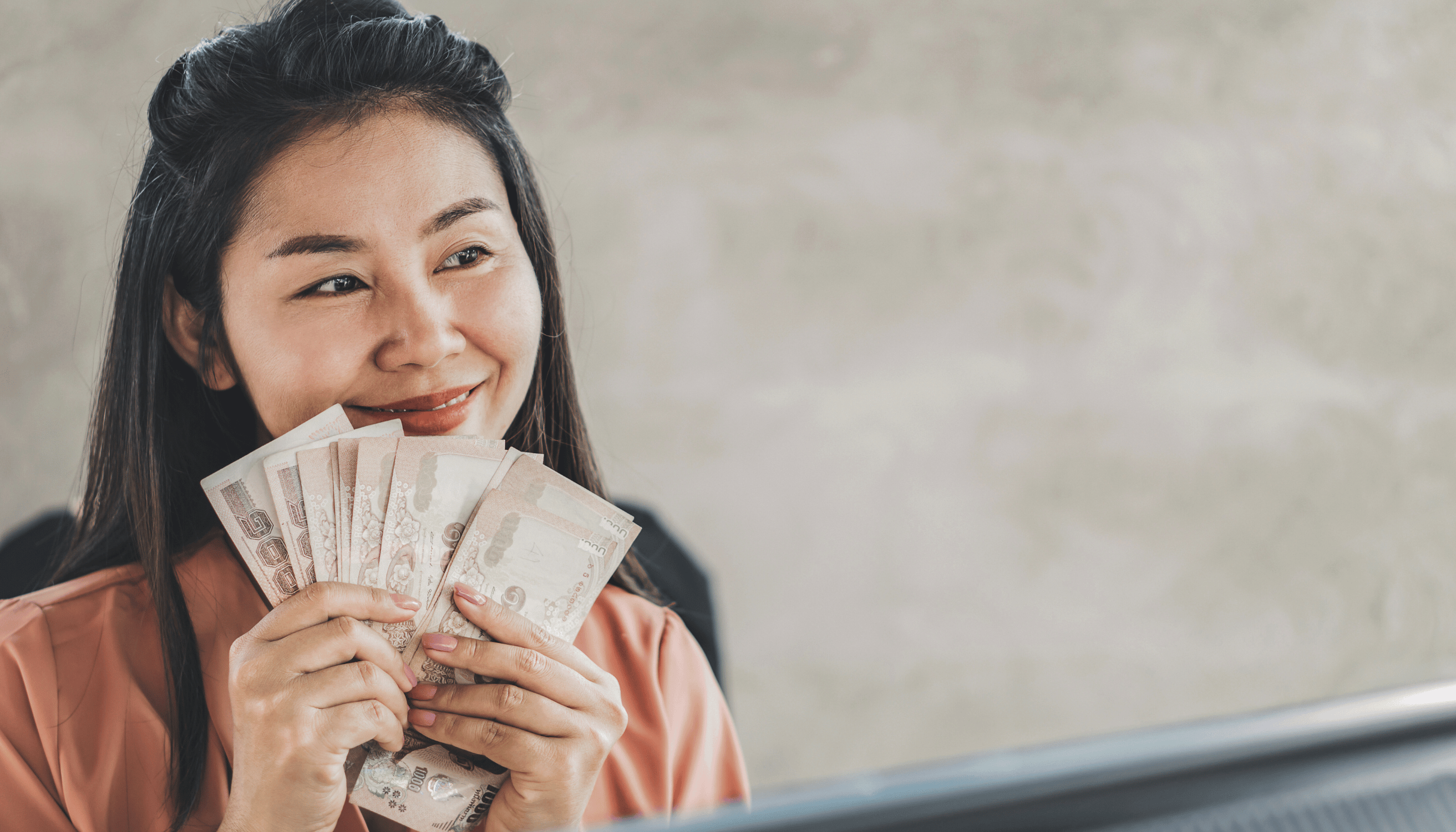 Smiling woman holding a stack of currency notes near her face, symbolizing currency echange or financial gains.