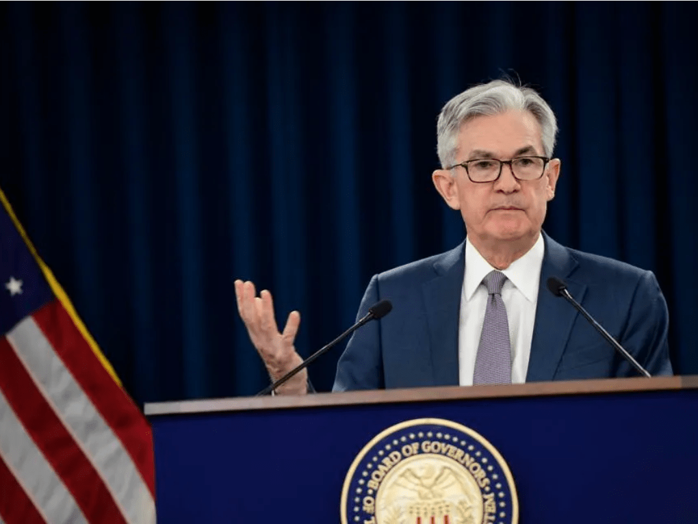 Federal Reserve Chair Jerome Powell delivers a speech at a press conference, addressing U.S. monetary policy and economic outlook, with an American flag in the background.